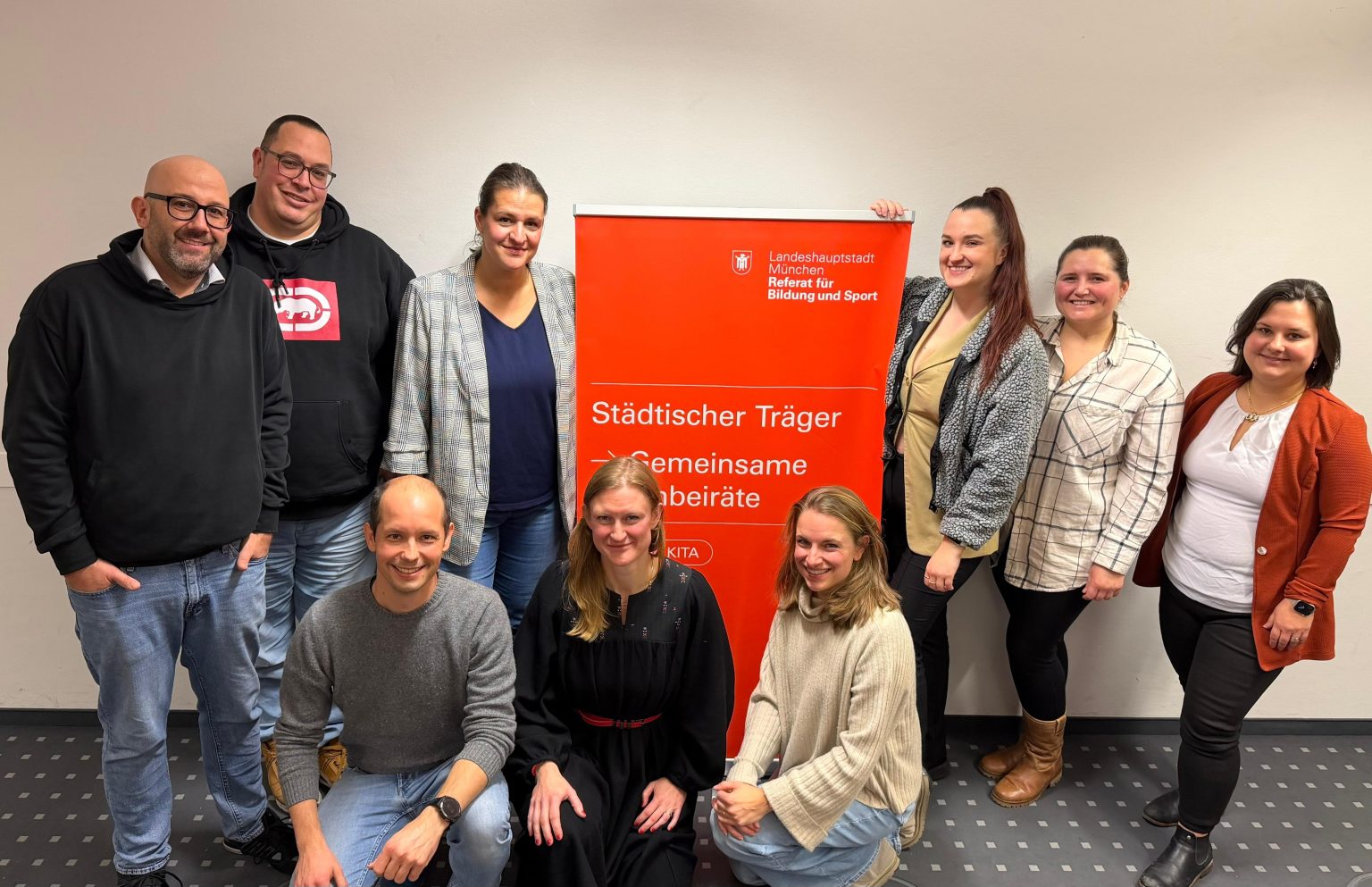 9 Mitglieder des GKB 2025/26 posieren nach der Wahl des Elternbeiratsgremiums vor einem roten Aufsteller